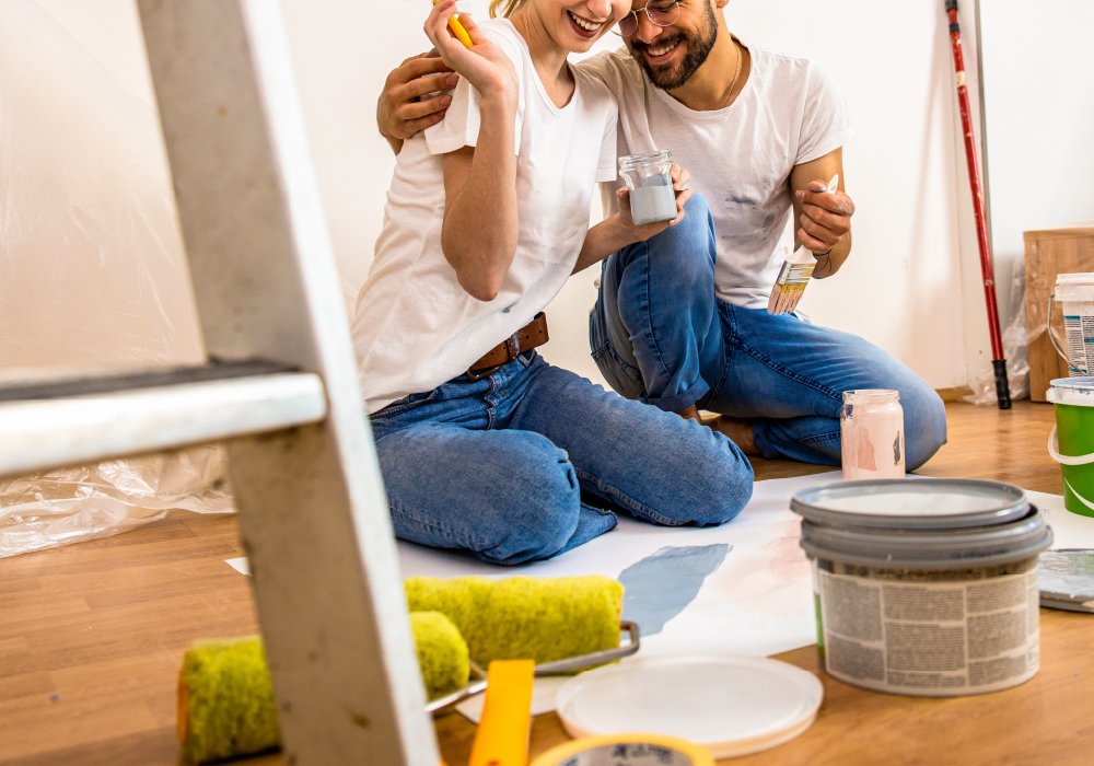 una ragazza e un ragazzo felici seduti sul pavimento intenti a ristrutturare casa con prodotti di Biella Legno